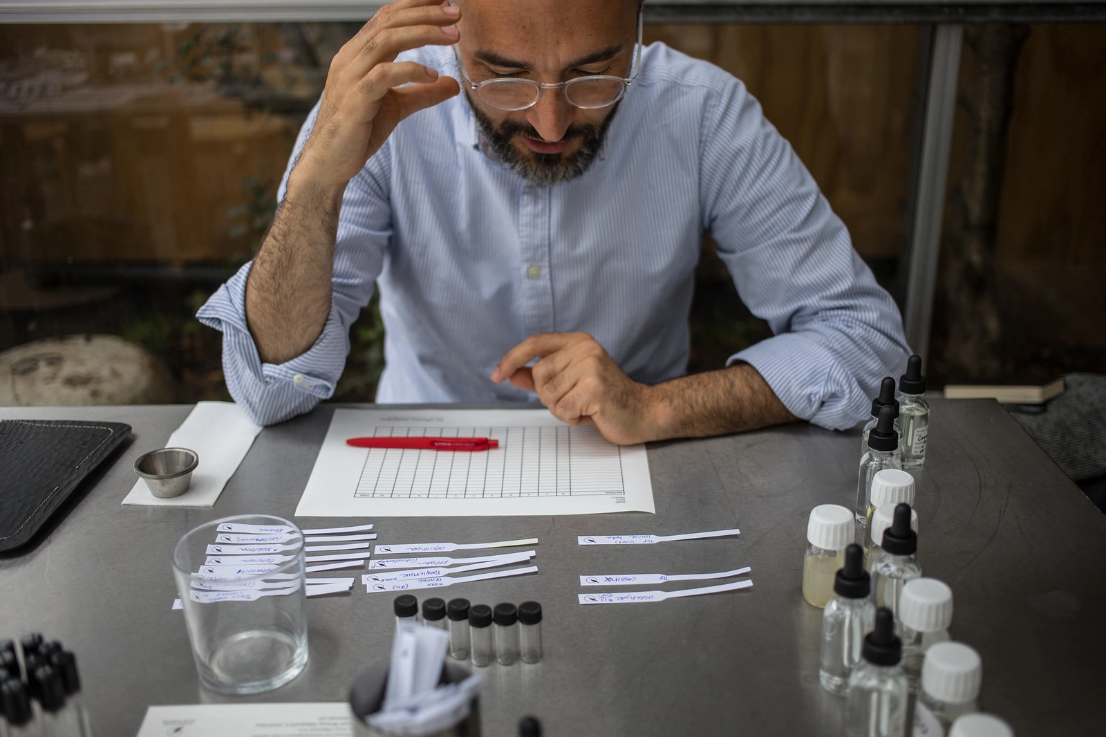 Un homme concentré remplit une fiche d’analyse sensorielle. Devant lui, plusieurs bandelettes et flacons odorants suggèrent une évaluation olfactive structurée.