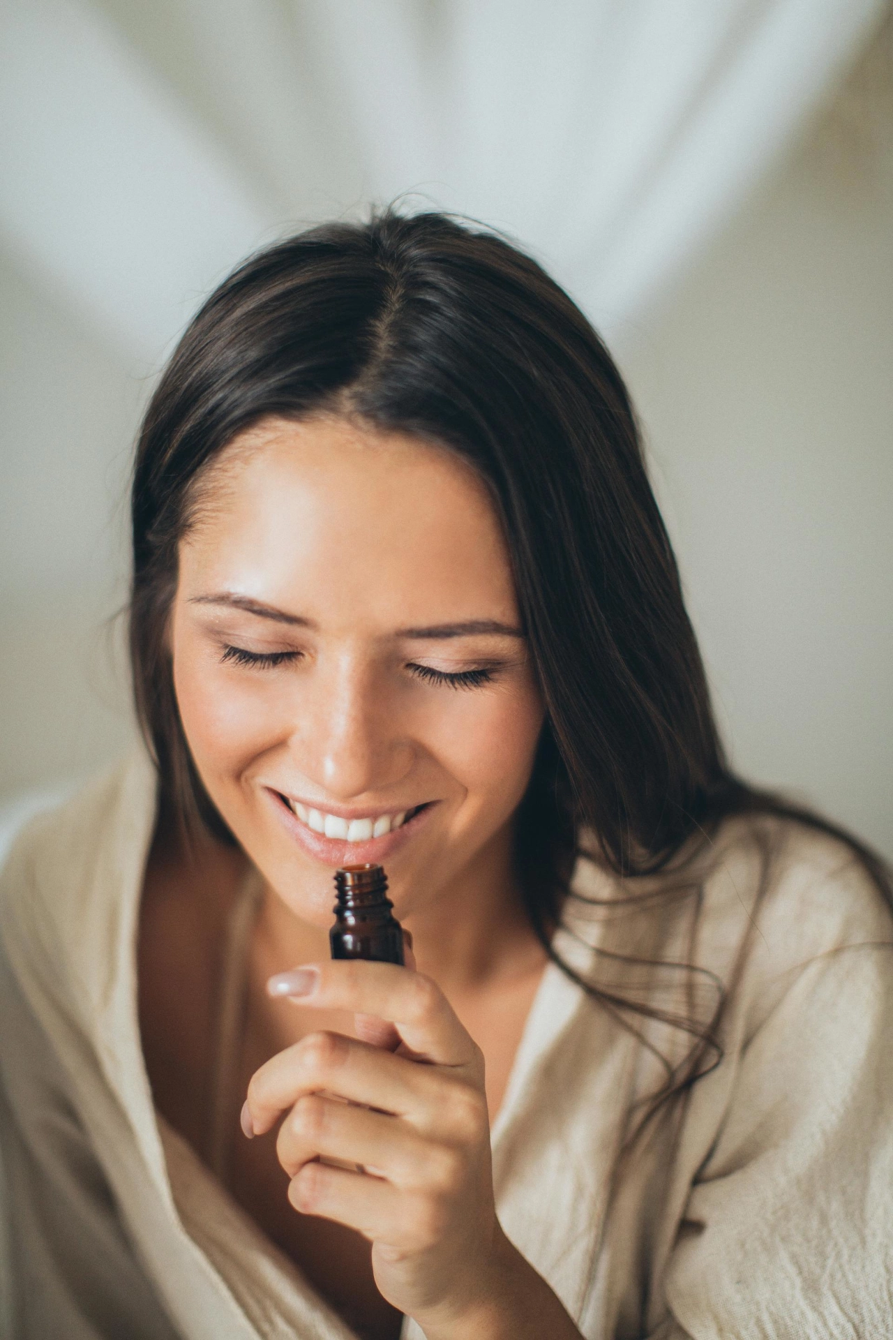 Femme souriante en train de sentir un flacon contenant une molécule odorante, illustrant une séance d’entraînement olfactif.
