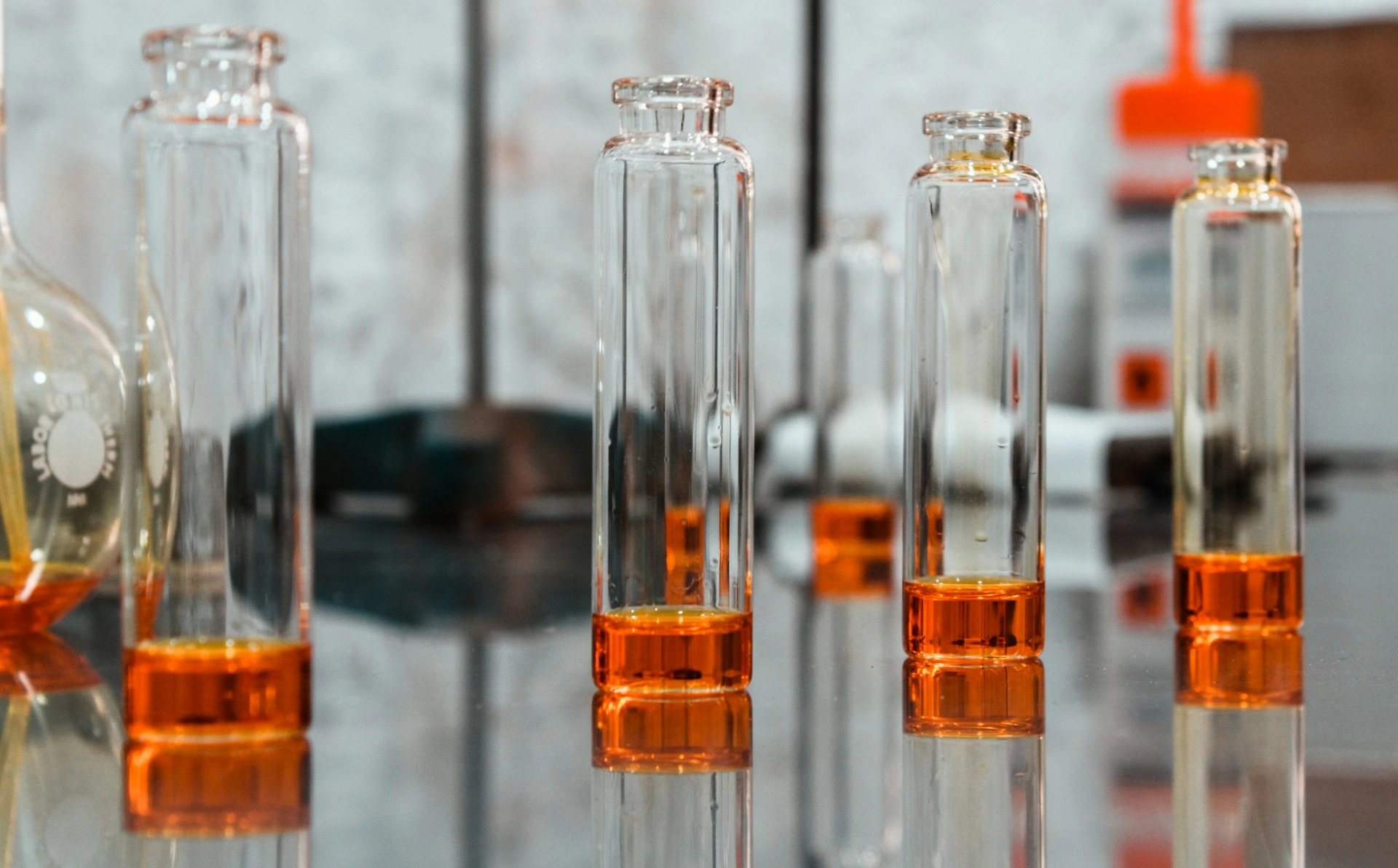 Photographie de plusieurs flacons contenant un liquide orange, évoquant des solutions de molécules odorantes utilisées dans des contextes d’analyse sensorielle ou d’entraînement olfactif.